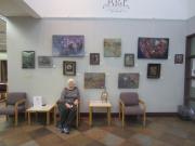 Photo of the artist with several paintings on the art wall.