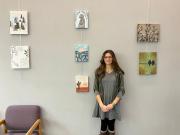 The artist standing with several canvases of her artwork on the wall.