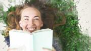 Photo of smiling girl reading book on grass