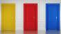 Photo of three closed doors, painted yellow, red and blue, set in a white wall.